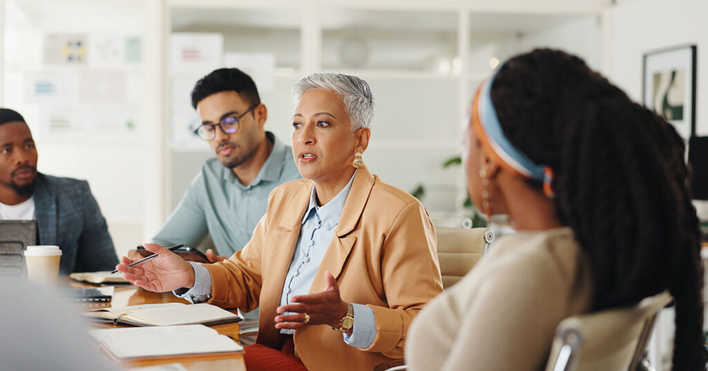 Woman at table in office speaking to a small group.